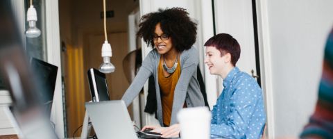 Two smiling people collaborate on a laptop at a desk