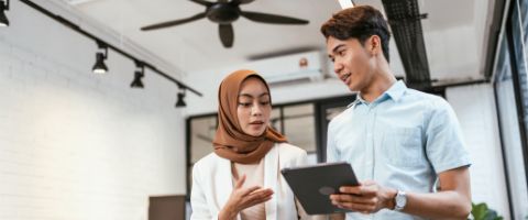 Two people walk together while discussing information shown on a tablet. 